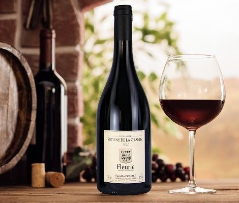 Fles Fleurie met gevuld glas en druiven, de vaten op de achtergrond